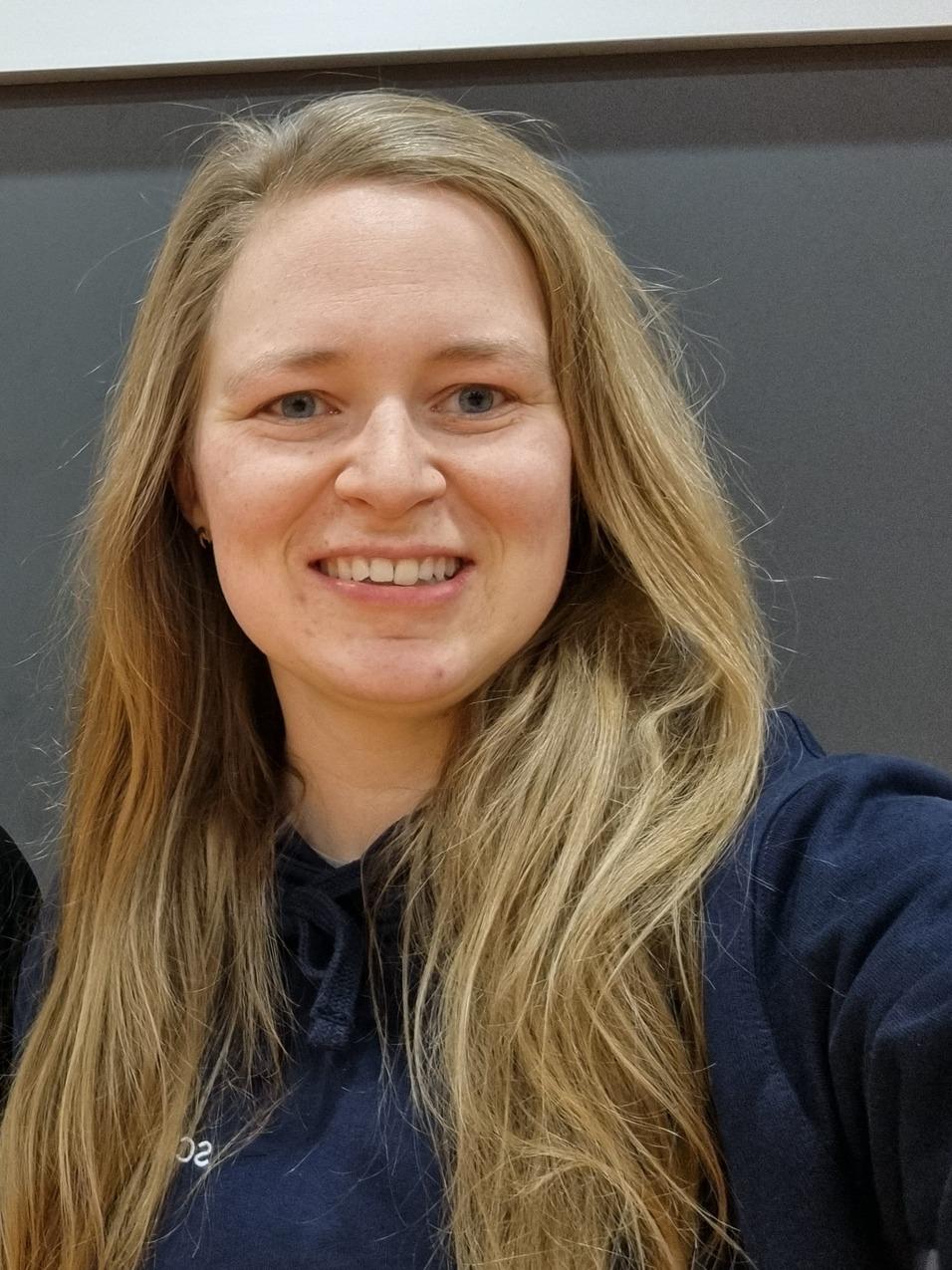 Zwei Frauen mit langen Haaren stehen lächelnd vor einer grauen Wand und posieren für ein Selfie.