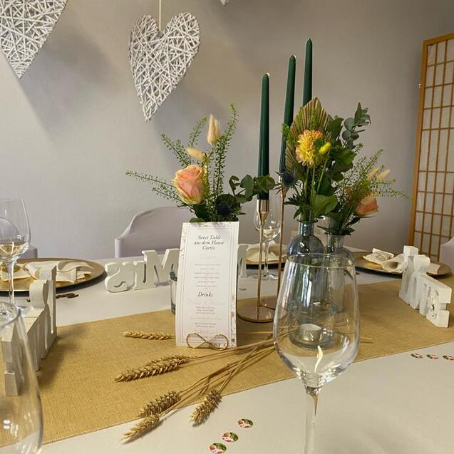Tischgedeck mit Gläsern, Blumenarrangement und Menükarten auf einem gedeckten Tisch in sanften Farben.