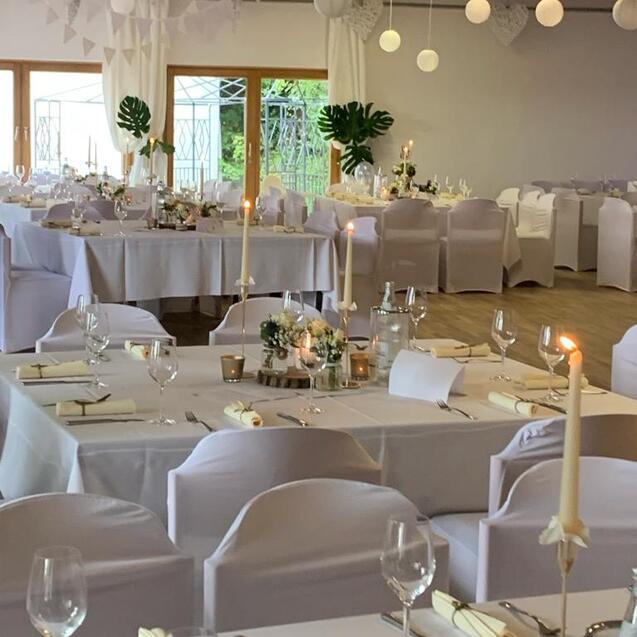 Elegant dekorierter Saal mit gedeckten Tischen, Kerzen und Blumenarrangements für eine festliche Veranstaltung.