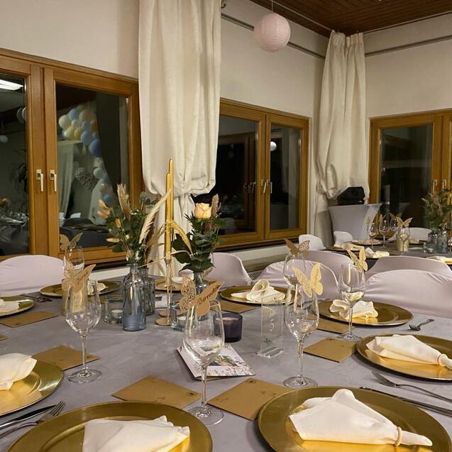 Elegant gedeckter Tisch mit goldenen Tellern, Gläsern und Blumenarrangements in einem festlichen Raum.