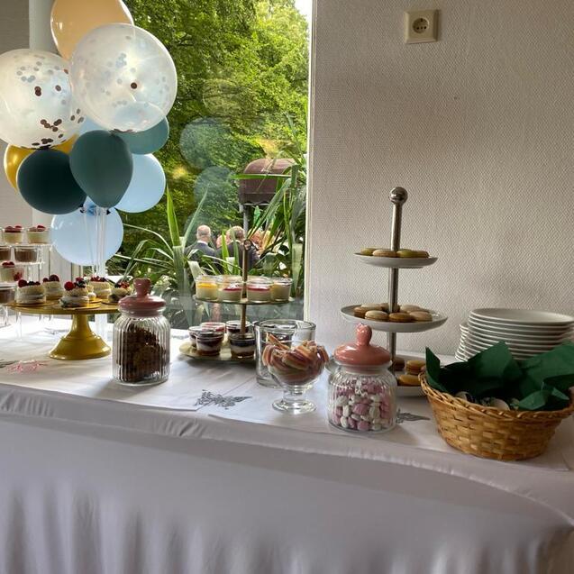 Buffet mit Gebäck, Süßigkeiten und dekorativen Ballons auf einem Tisch in einem Garten.