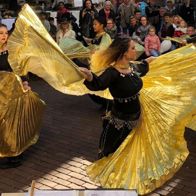 T&auml;nzerinnen in goldenen Kost&uuml;men f&uuml;hren eine Darbietung auf einem Platz vor einem begeisterten Publikum auf.