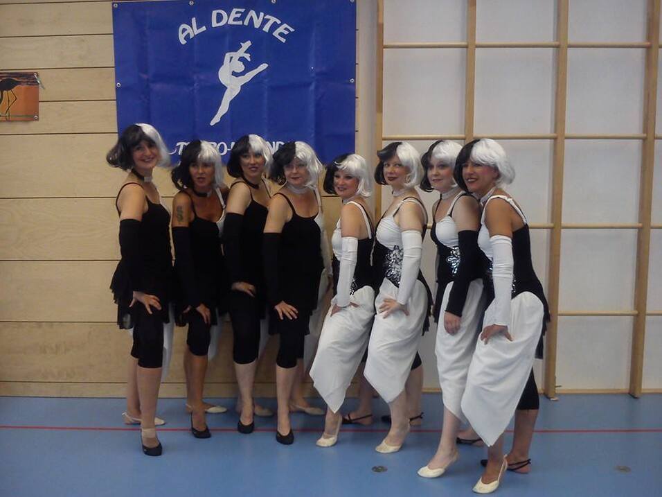 Gruppe von T&auml;nzerinnen in schwarz-wei&szlig;en Kost&uuml;men posiert vor einem Banner mit der Aufschrift "AL DENTE".