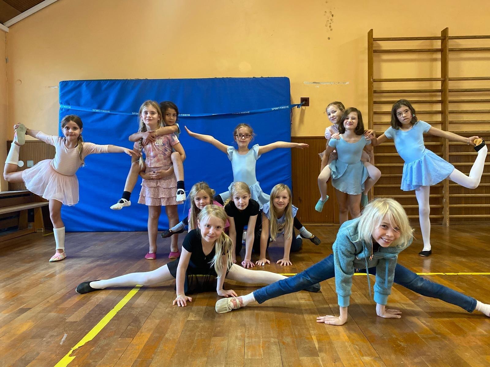 Gruppe von M&auml;dchen in Ballettkleidung, die verschiedene Posen in einem Tanzraum einnehmen.