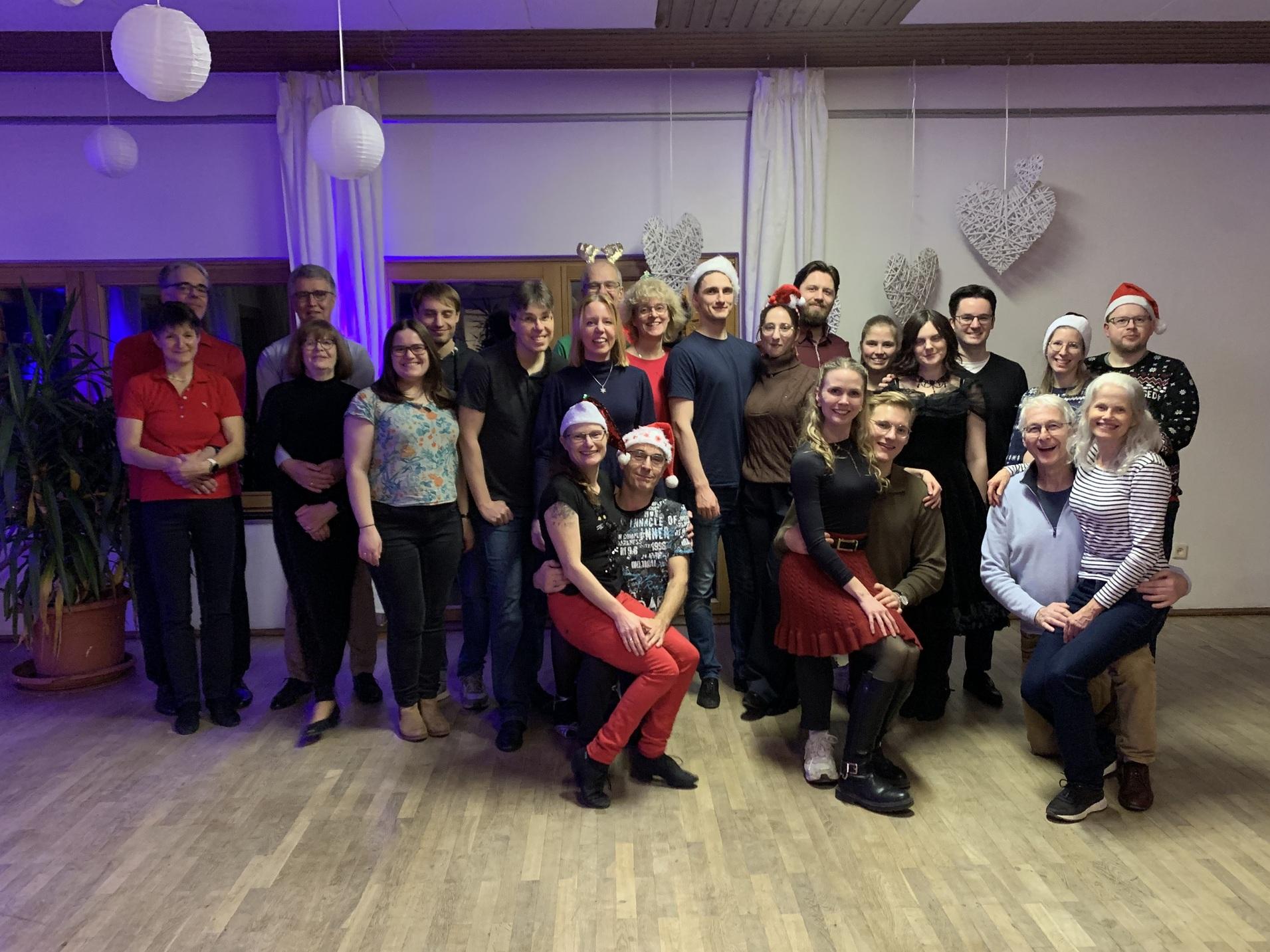 Gruppe von 22 Personen in festlicher Kleidung, versammelt in einem Raum mit dekorativem Licht und Weihnachtsdekoration.