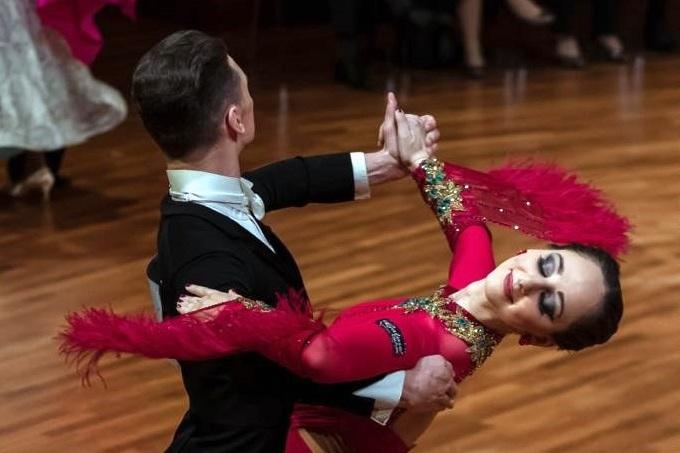 Tanzpaar in festlicher Kleidung f&uuml;hrt eine elegante Drehung auf der Tanzfl&auml;che vor Publikum aus.