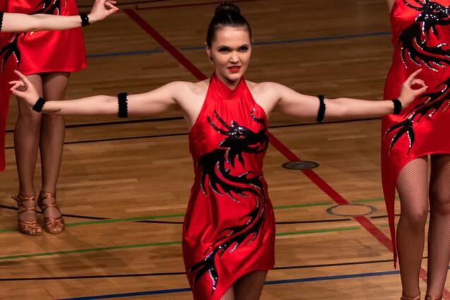 T&auml;nzerin in rotem Kleid mit schwarzen Verzierungen, die in einem Sporthalle auf einer B&uuml;hne posiert.