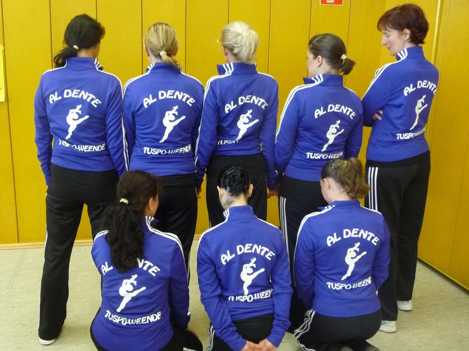 Gruppenshot von sieben Frauen in blauen Sportjacken mit dem Aufdruck "AL DENTE TUSPUENDE", von hinten fotografiert.