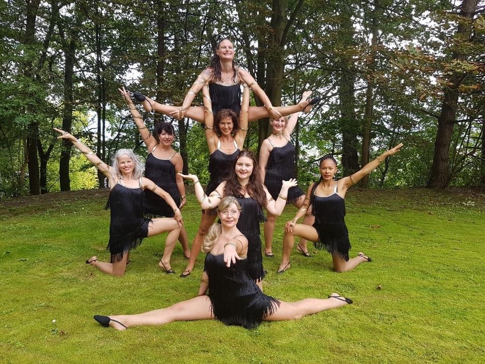 Gruppe von T&auml;nzerinnen inFransenkleidung, posierend in harmonischer Formation auf einer gr&uuml;nen Wiese.