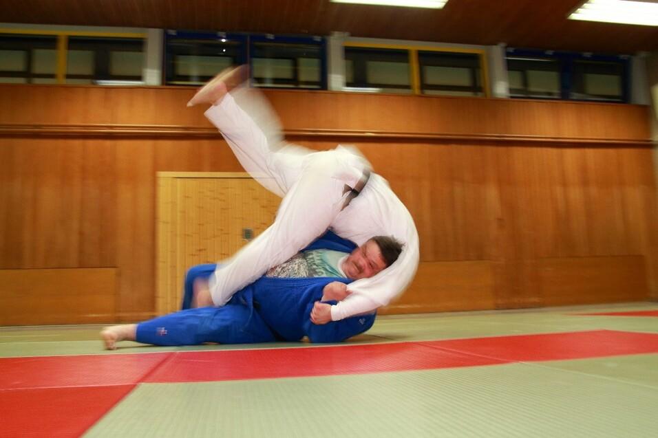 Zwei Judokas in einem Kampf: Ein K&auml;mpfer mit wei&szlig;em Anzug wirft einen Gegner im blauen Anzug auf eine Matte.