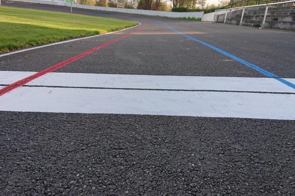 Nahaufnahme einer Rennstrecke mit wei&szlig;en, roten und blauen Linien auf schwarzem Asphalt und gr&uuml;nem Rasen im Hintergrund.