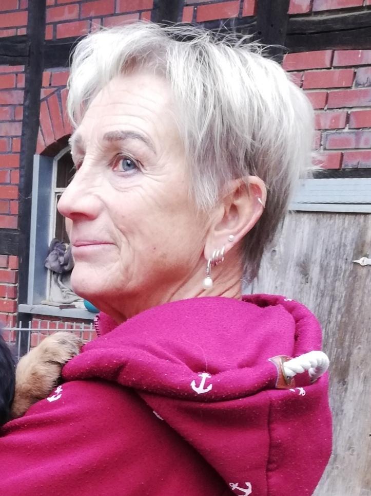 Frau mit kurzem Haar hält einen schwarzen Welpen in einem verschneiten, ländlichen Umfeld.