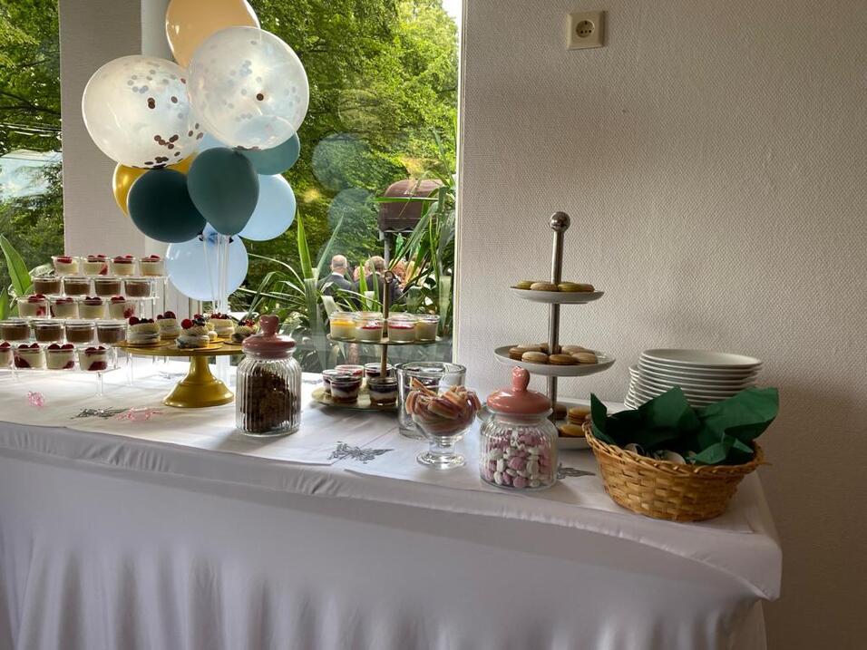 Buffet mit verschiedenen s&uuml;&szlig;en Leckereien, darunter Cupcakes, Pl&auml;tzchen und Ballons, auf einem wei&szlig;en Tisch.