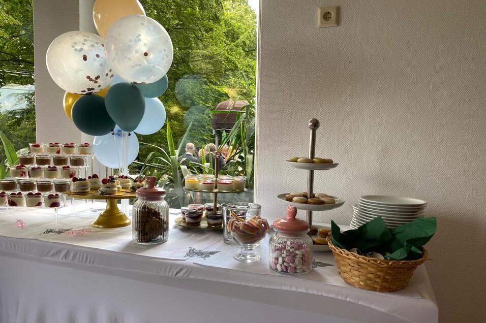 Buffet mit verschiedenen süßen Leckereien, darunter Cupcakes, Plätzchen und Ballons, auf einem weißen Tisch.