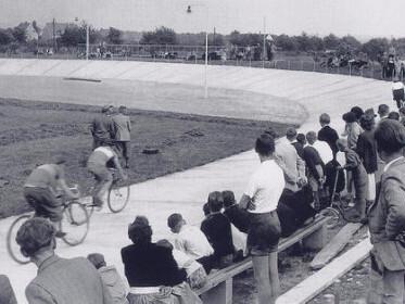 Zuschauer beobachten Radrennen auf einer Velodrombahn in schwarz-weiß. Velofahrer in Aktion auf der Strecke.