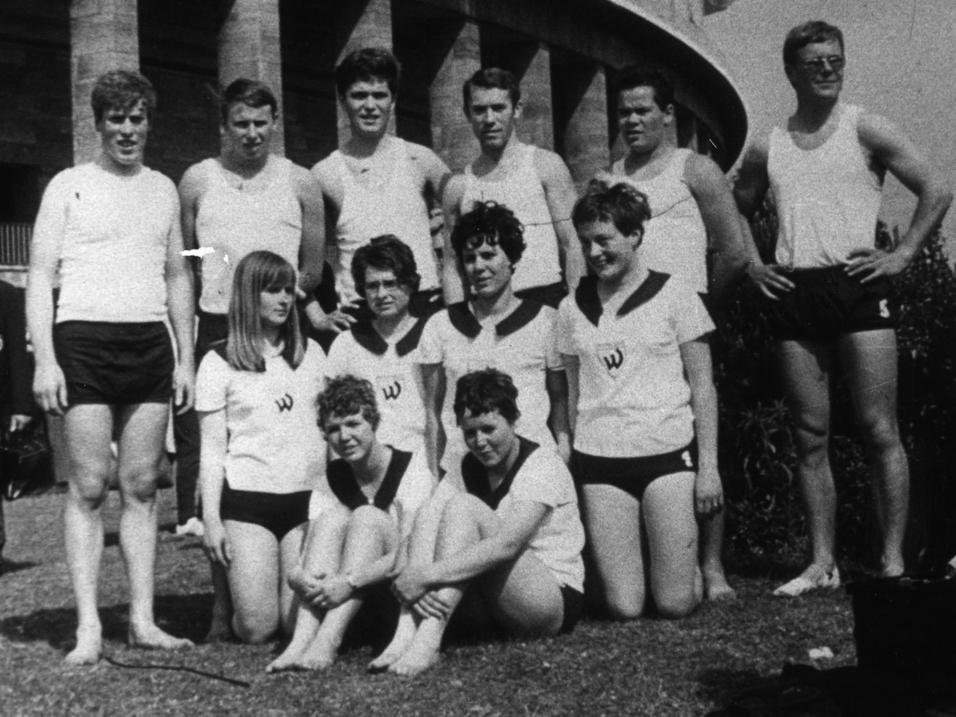 Gruppe von fünf Männern und fünf Frauen in Sporttrikots auf einer Wiese vor einem Bauwerk.