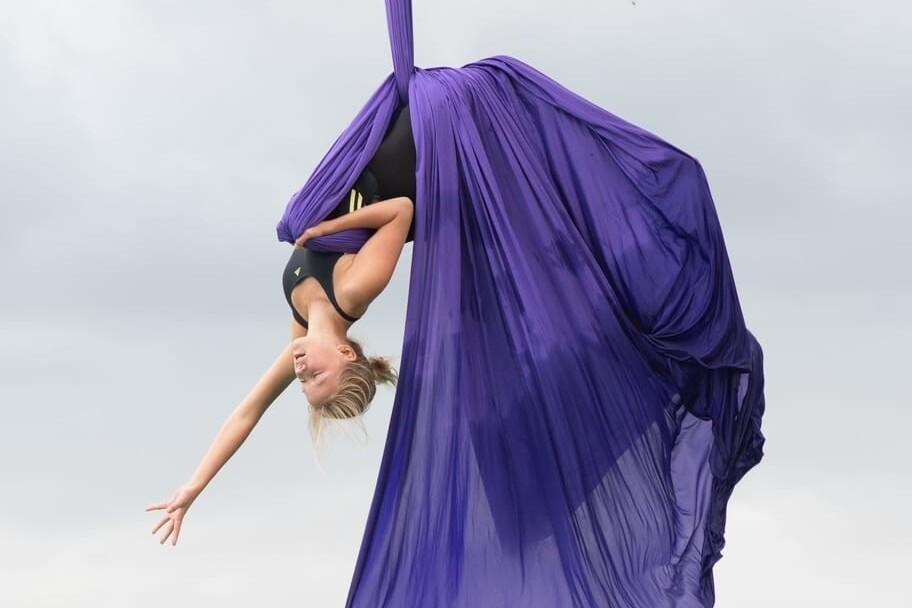 Tänzerin in lila Tuch schwingt kopfüber in der Luft.