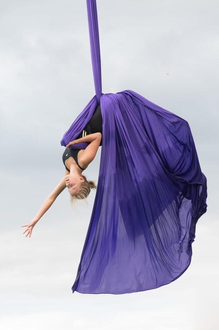 T&auml;nzerin in lila Tuch schwingt kopf&uuml;ber in der Luft.