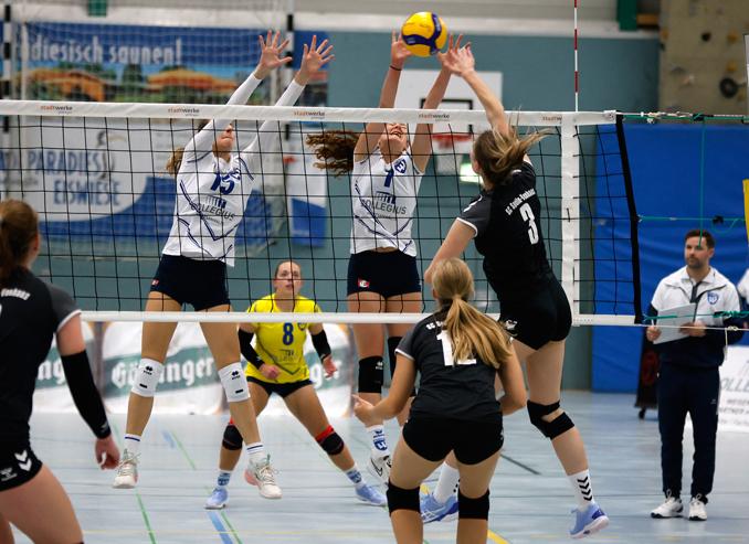 Zwei Volleyballspielerinnen blocken einen Ball am Netz, w&auml;hrend eine gegnerische Spielerin anl&auml;uft, um zu schlagen.