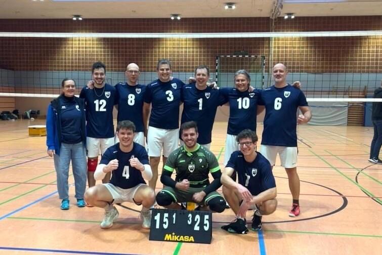 Vor einer Volleyball-Spielfeld steht ein Team aus neun Spielern in blauen Trikots, posierend mit Punktezähler.