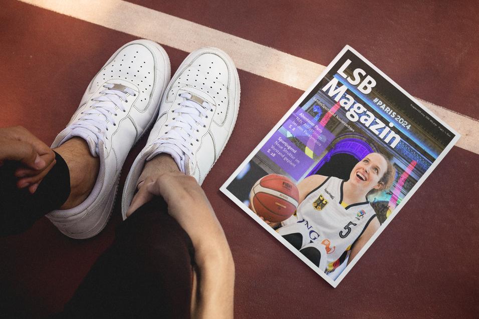 Nahaufnahme eines Fu&szlig;es im Sneaker neben einem Magazin auf einem Basketballplatz. Das Magazin zeigt eine Basketballspielerin.