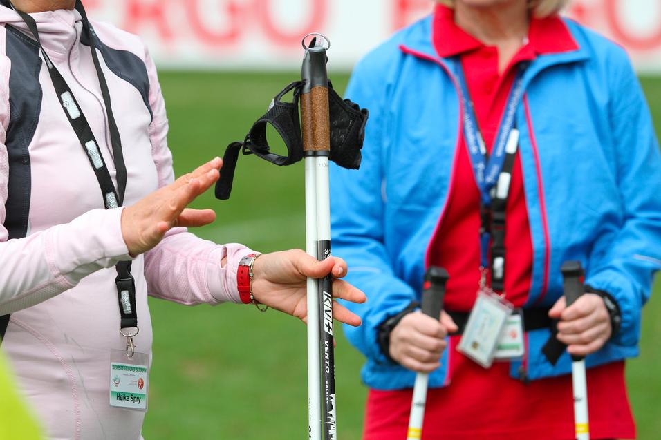 Zwei Frauen stehen auf einer Wiese, eine zeigt auf einen speziellen Stock für Blinde mit Halterung.