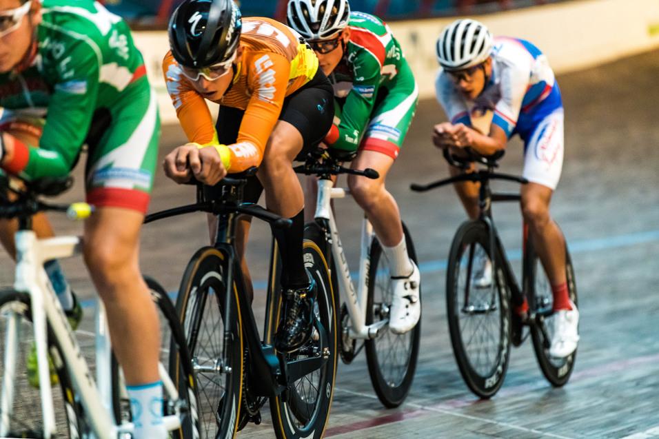 Vier Radfahrer in Wettkampfposition fahren auf einer Bahn, während sie sich um die Führung bemühen.